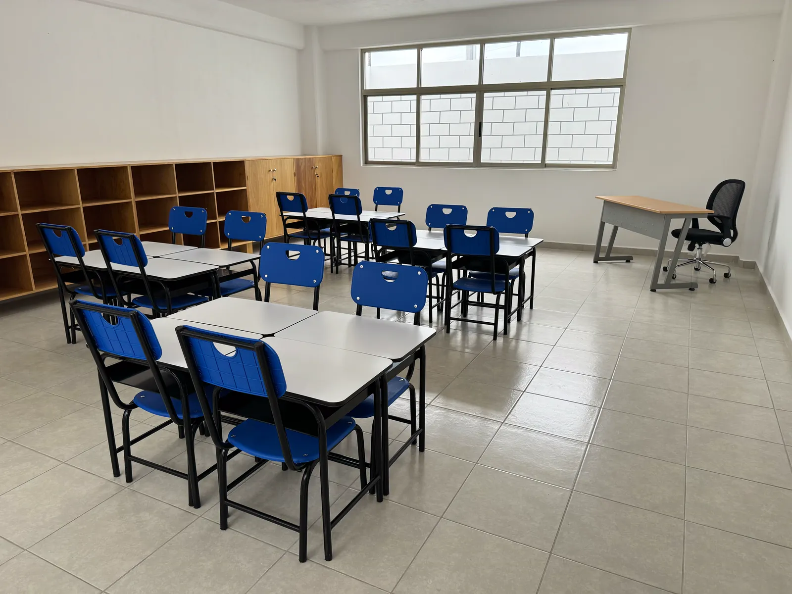 Salón con mesas para trabajo en equipo y escritorio del docente